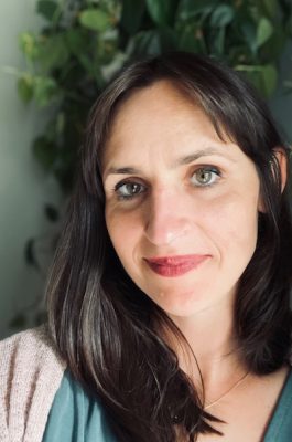 A woman poses for a headshot in front of a plant.