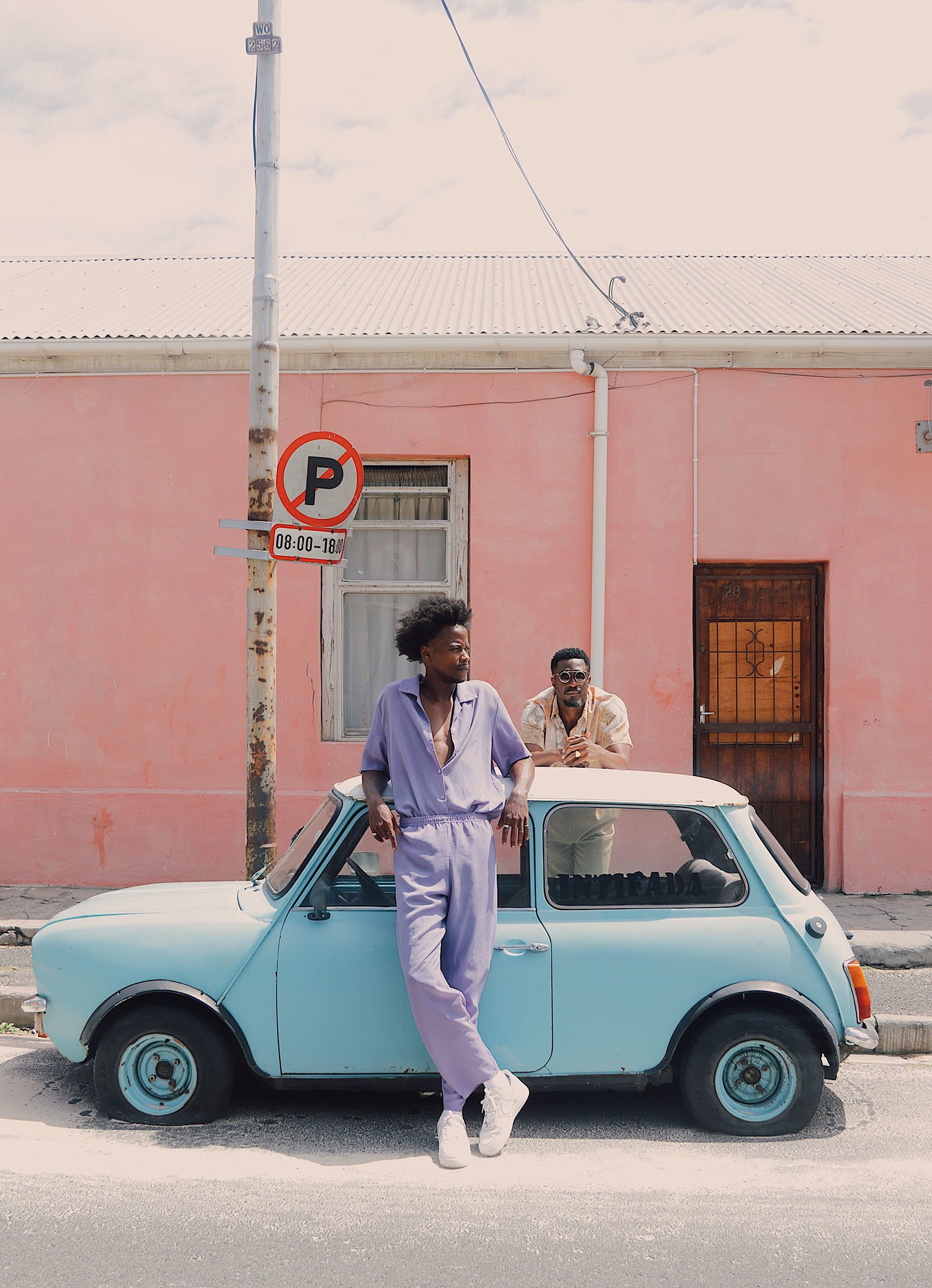 A person dressed in lavender leans against a small light blue car.