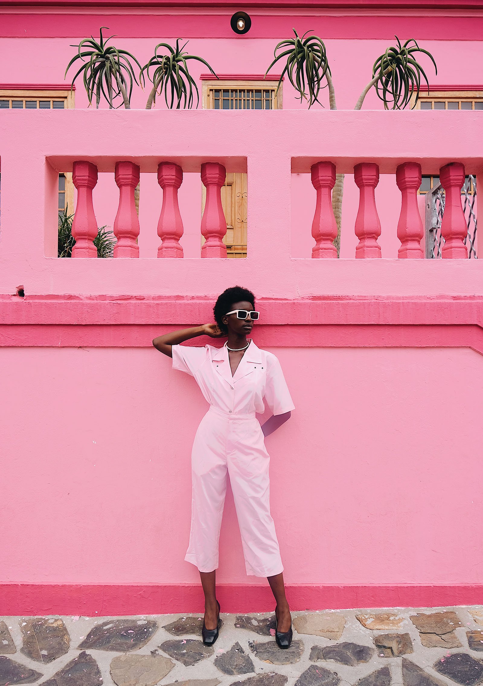 A woman in light pink poses against a darker pink wall.