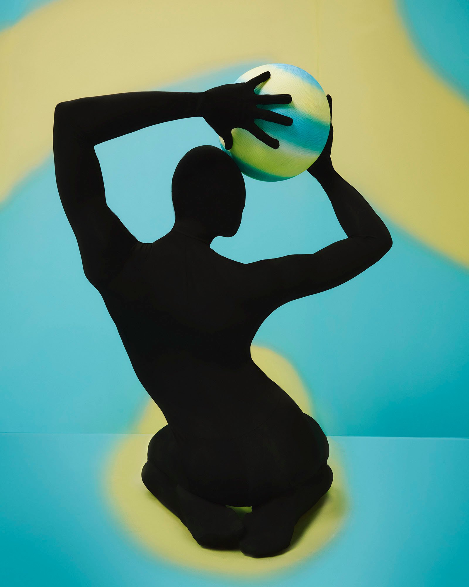 A silhouette holds a ball overhead.