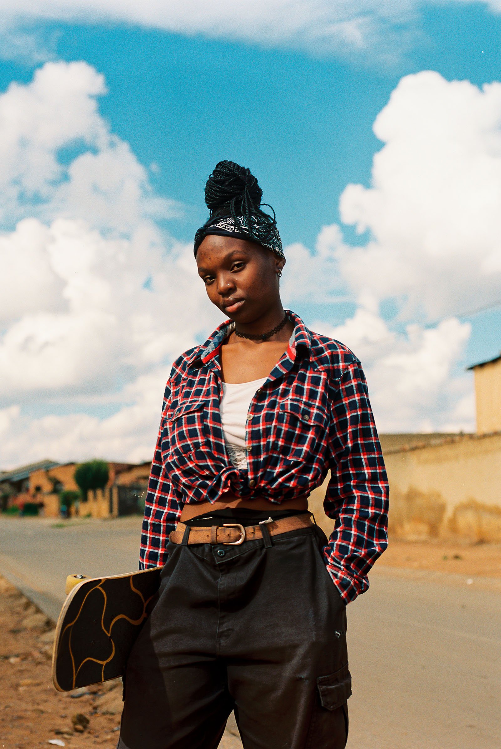 A girls stands by a road with a skateboard.