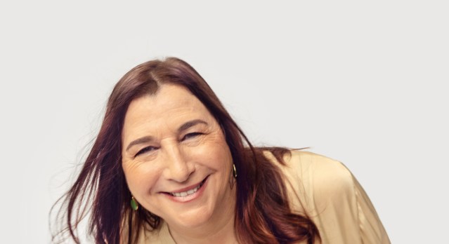 Jana Jerzen smiling at the camera leaning in, against a plain off-white background