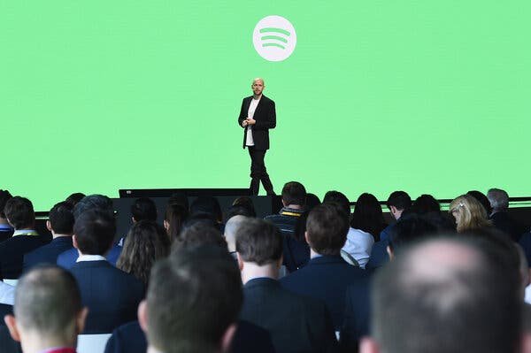 Daniel Ek, wearing a dark coat and white shirt, speaks to a crowd in front of a large green screen.