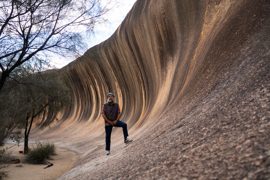 man in front of giant wave rock