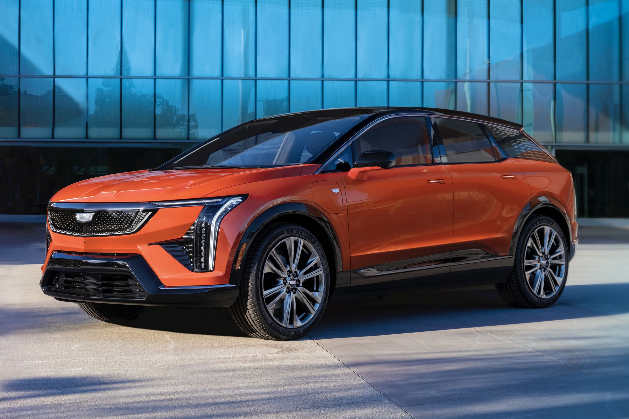 Orange Cadillac SUV with black painted top in front of a glass panel building