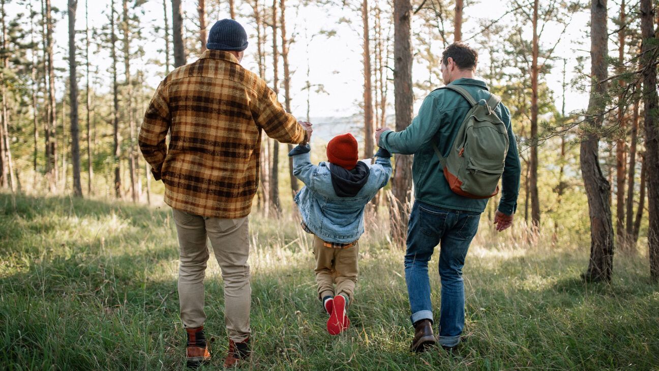 Two man and girl in red hat walk in a forest.