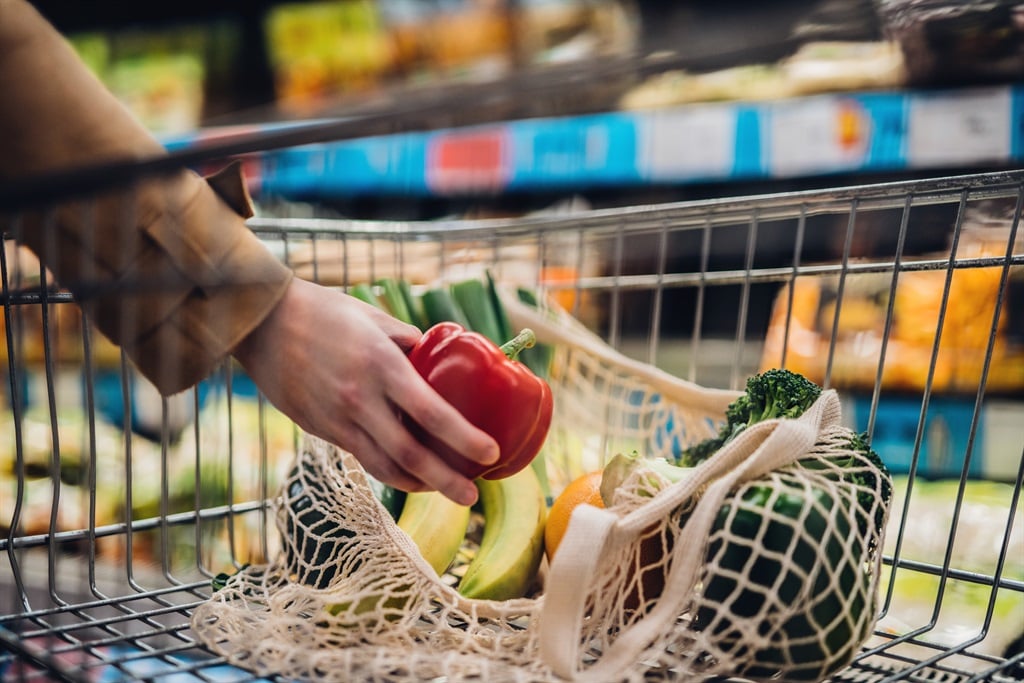 Illustration: Close-up shot of female hand putting a red bell pepper into a mesh grocery bag. 