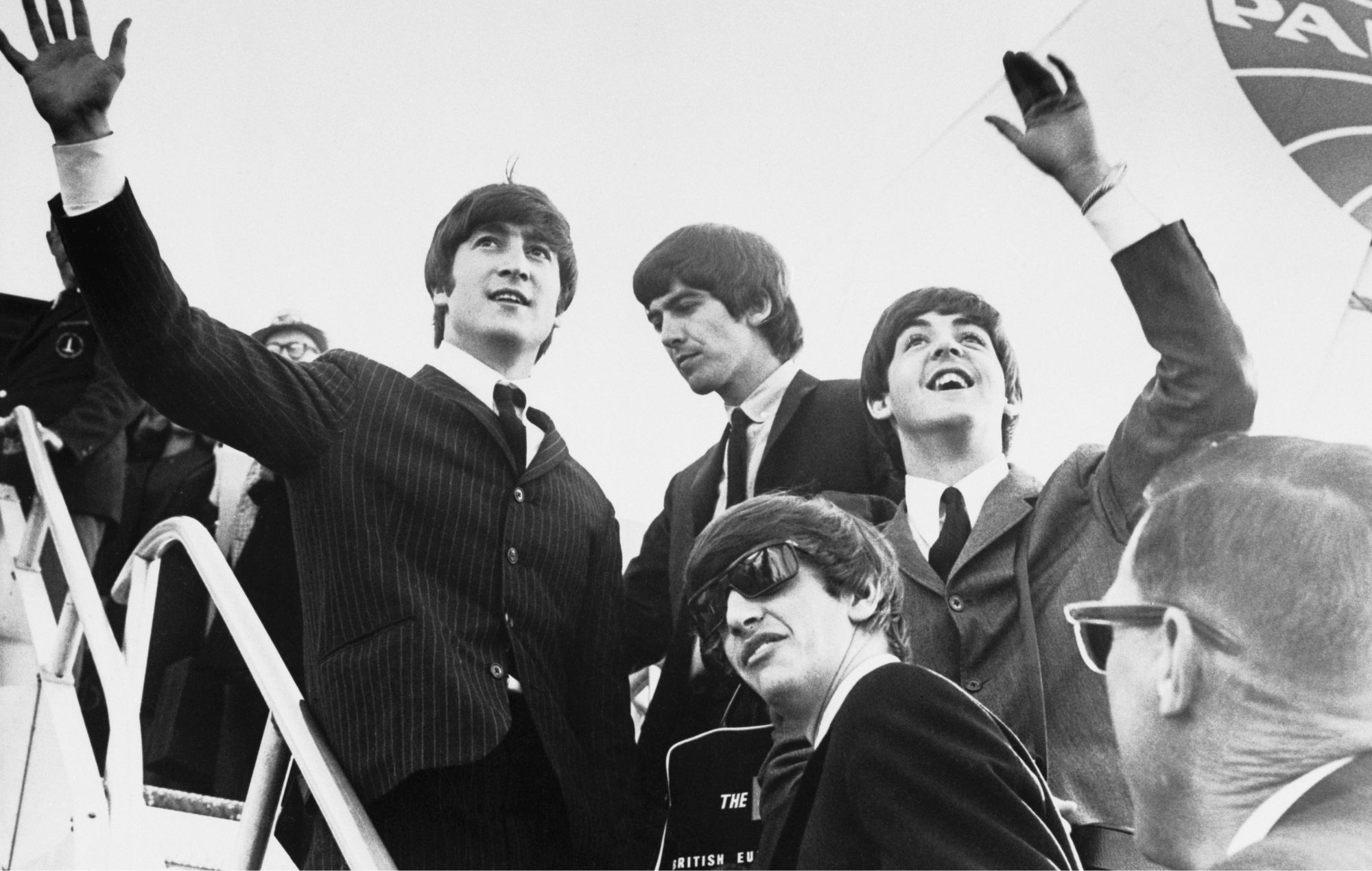 The Beatles - John Lennon, George Harrison, Paul McCartney, and Ringo Starr (foreground) - wave to several hundred screaming fans before climbing aboard their airplane and leaving Miami.