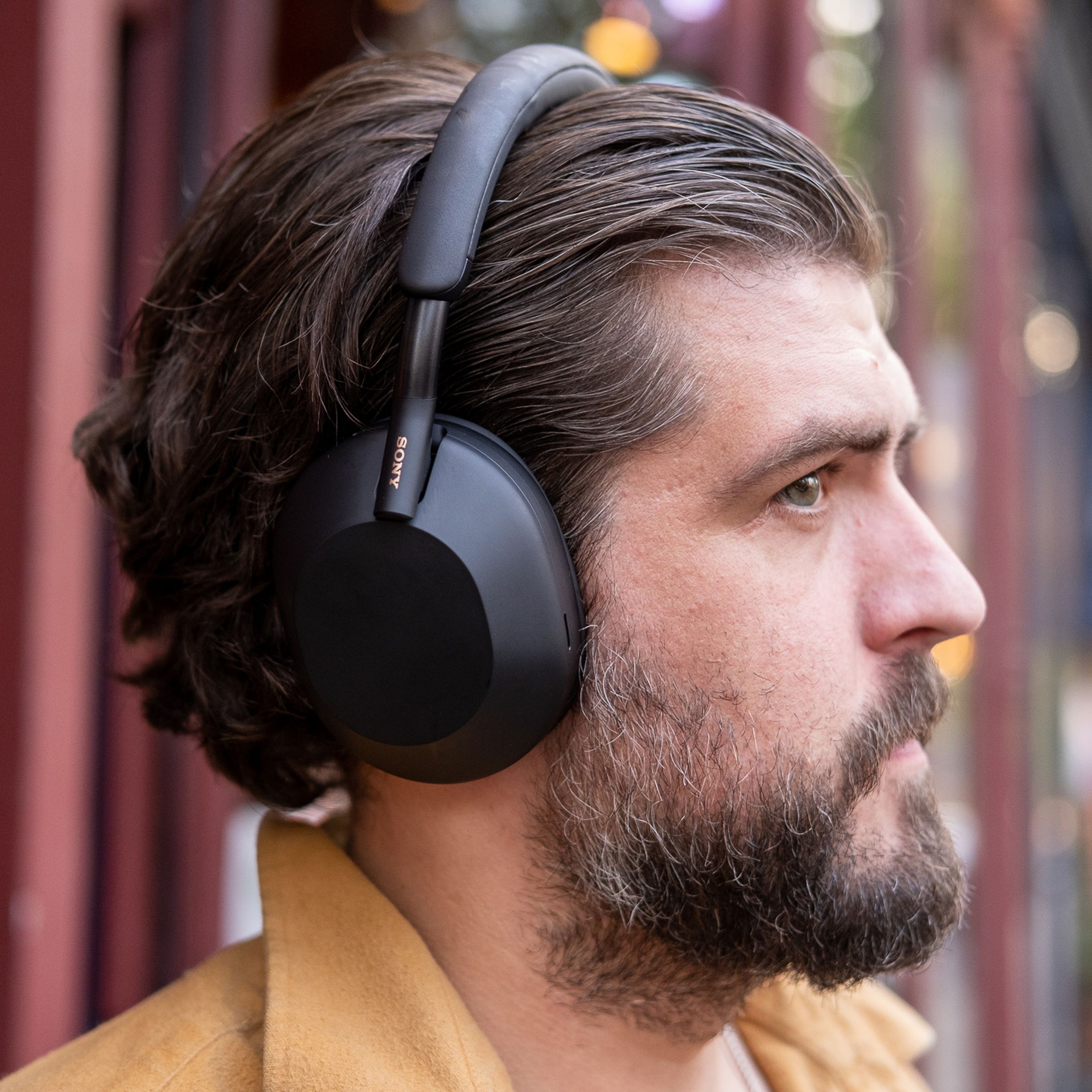 A man wearing Sony’s black WH-1000XM5 noise-canceling headphones outside.