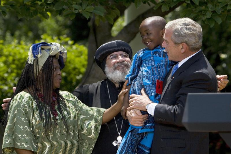 Then-U.S. President George W. Bush holds Baron Mosima Loyiso Tantoh as Tantoh's mother Manyongo Mosima Kuene Tantoh (L), who suffers from AIDS, and Bishop Paul Yowakim (2nd L) looks on after speaking on the President's Emergency Plan for AIDS Relief May 30, 2007 at the White House in Washington.