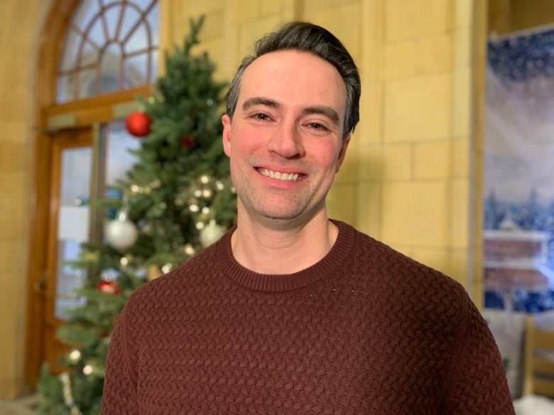 A man wearing a burgundy sweater poses for a photo in front of a holiday display.