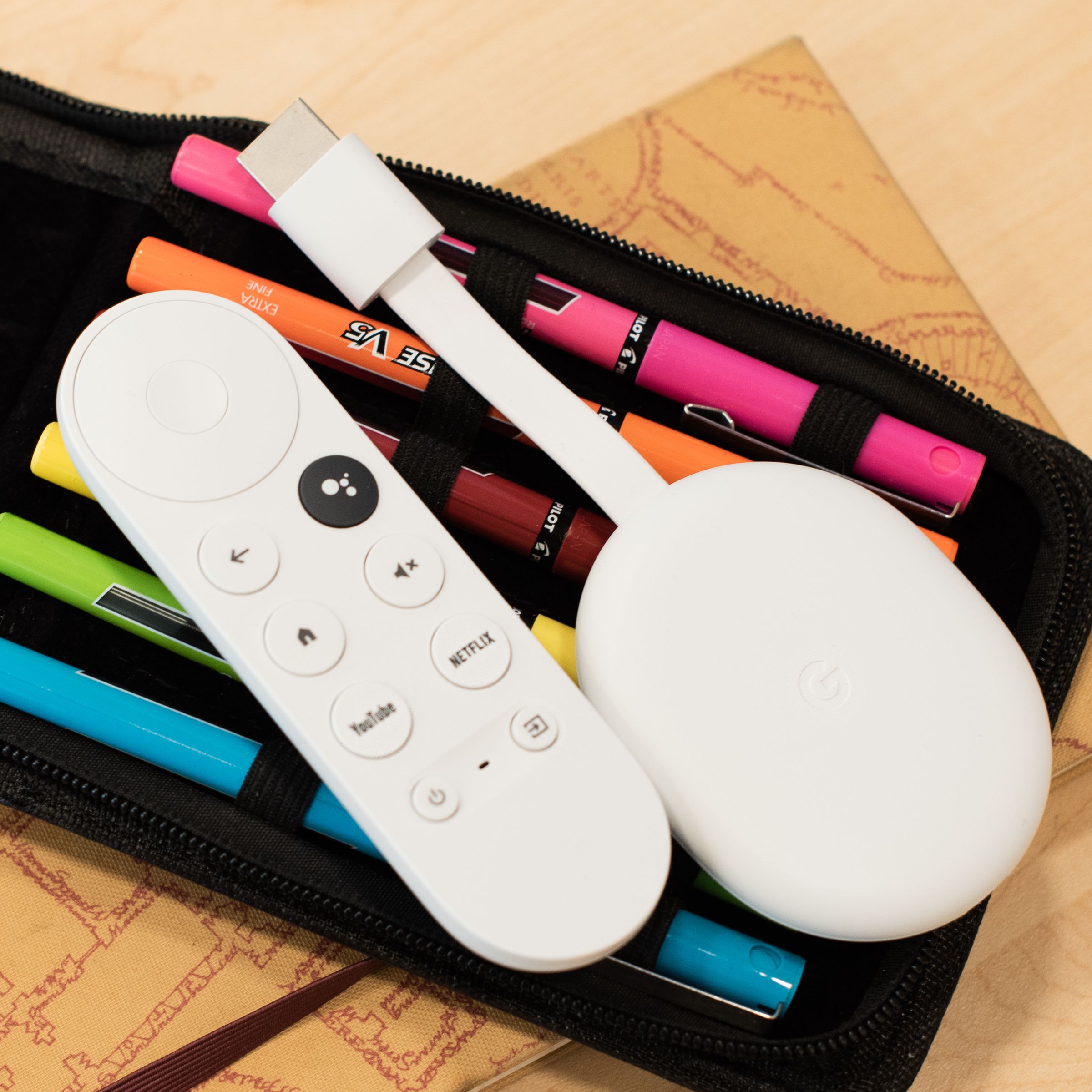 The Chromecast with Google TV (4K) with its remote lying on a pack of pens.