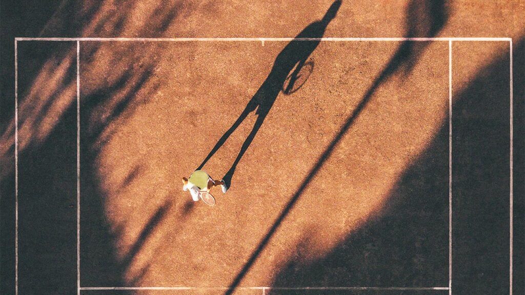 A drone view of a person on a tennis court outside under the sun