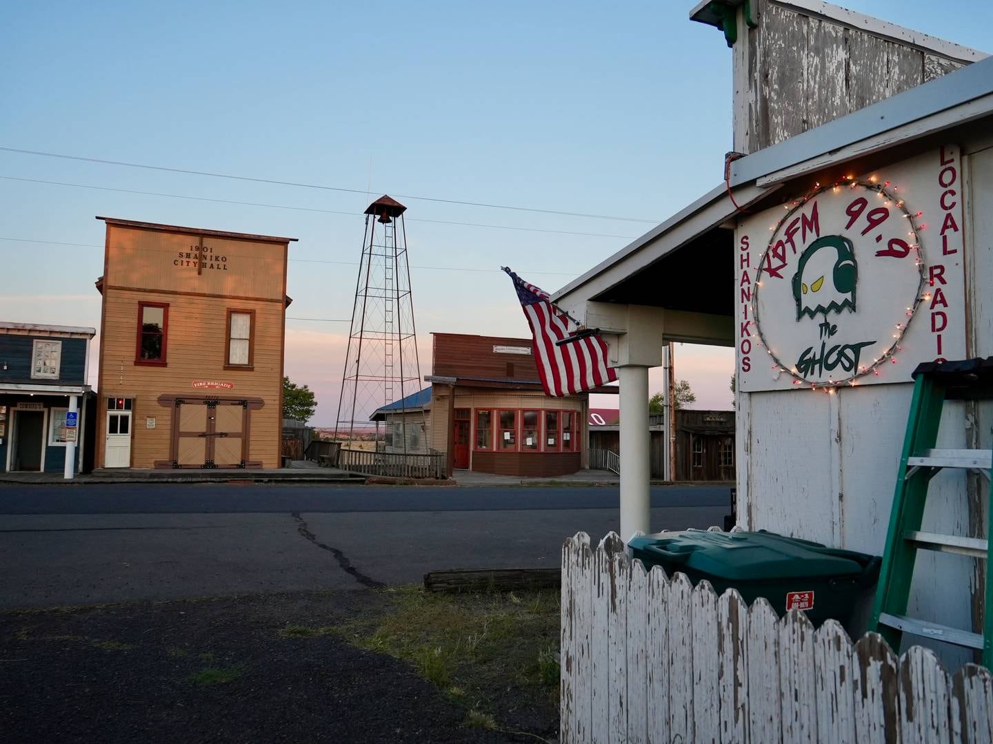 side view of a wood building with the sign that says KDFM 99.9 The Ghost, an American flag hangs on front of the building and across the street we see some old west style buildings