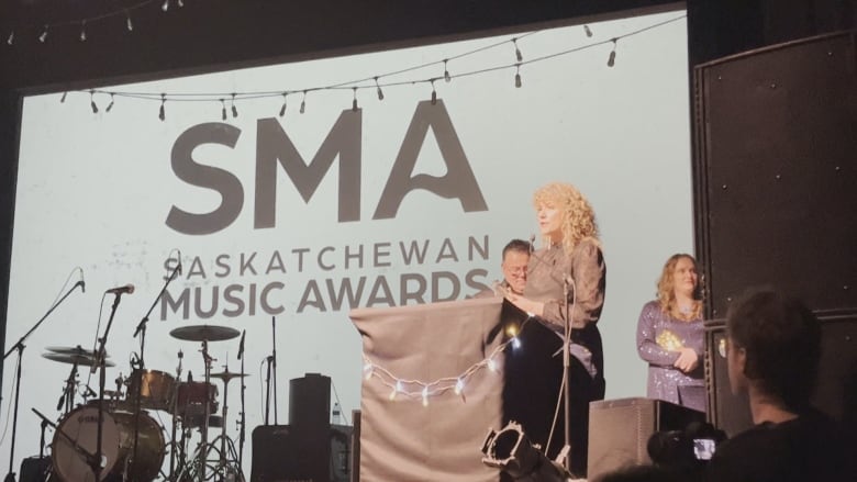 Alexis Normand is on a stage with musical instruments and backdrops with Saskatchewan Music Award logos on it