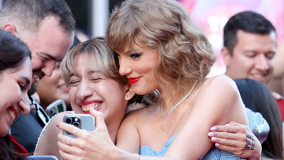 Taylor Swift in a blue strapless dress being embraced by fans