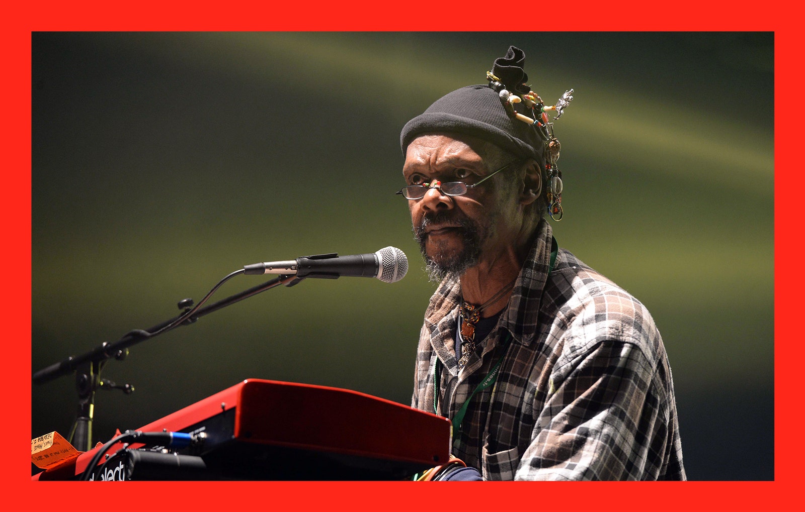 US singer Lonnie Holley performs on stage wearing a hat and a plaid shirt.