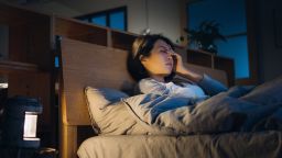 Young Asian woman feeling sick and suffering from a headache, lying on bed and taking a rest at home