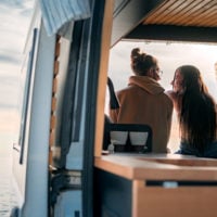 Ein Paar sitzt auf der Schwelle des Vans mit Blick auf Wasser