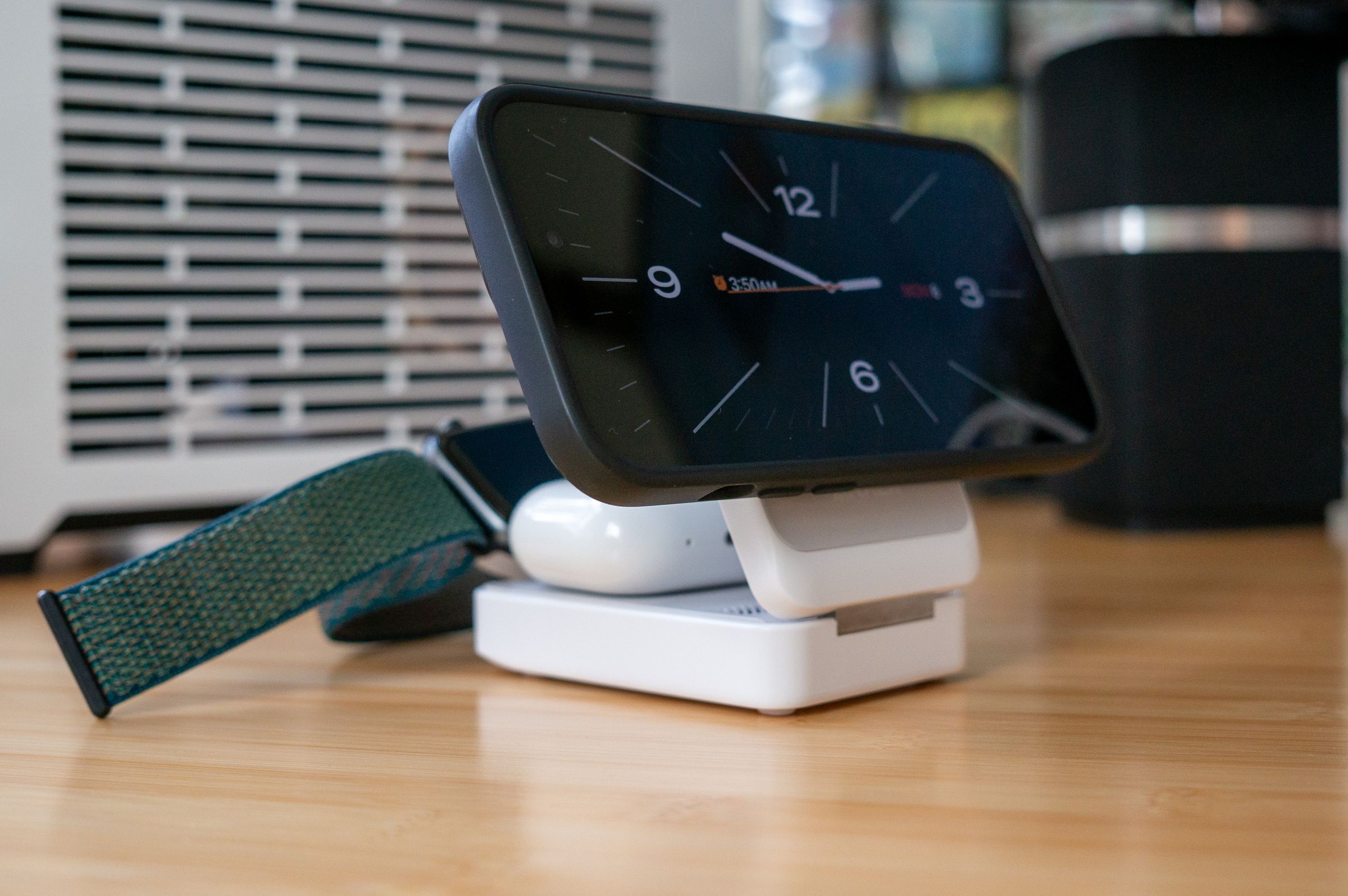 An iPhone 14, Apple Watch, and AirPods Pro all charging on a white portable Qi2 charger. The Apple Watch puck flips up from underneath.