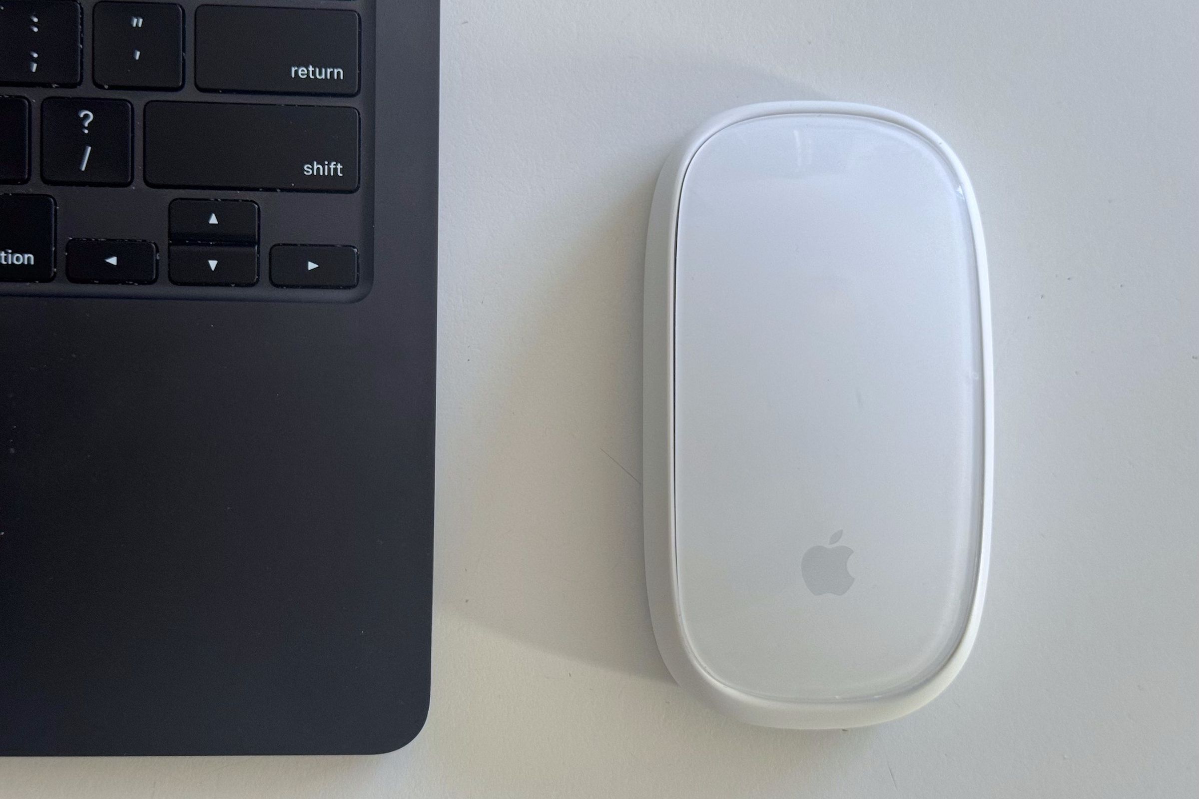 A picture of the Magic Mouse 2 in the wireless charging grip, sitting next to a MacBook Air.