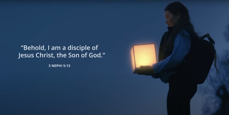 A young woman wearing a backpack holds a rectangular lantern and the theme scripture is printed on the left.