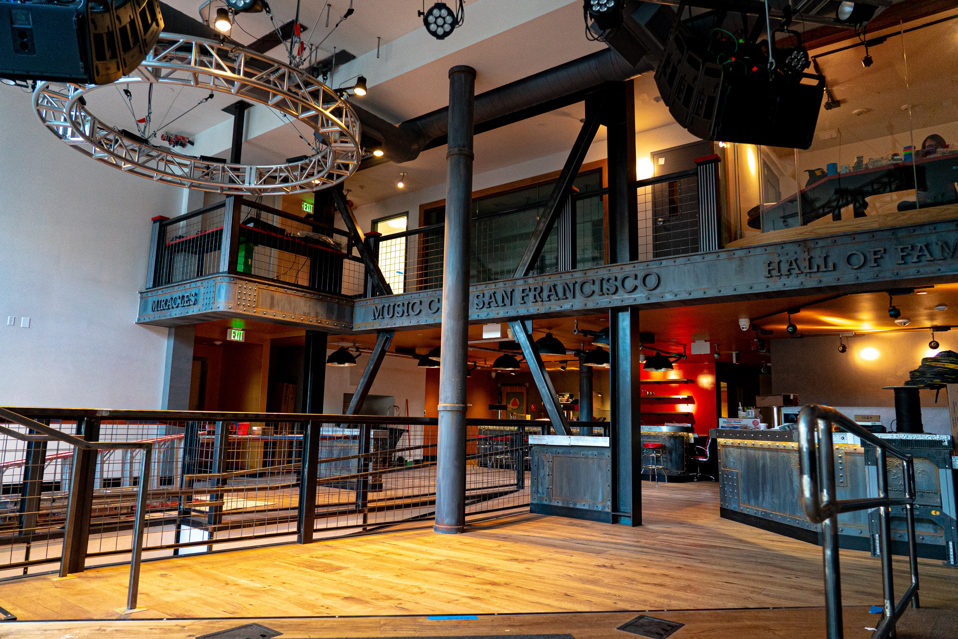 A warehouse-looking space has a bar in the back and wooden floors with black columns. 