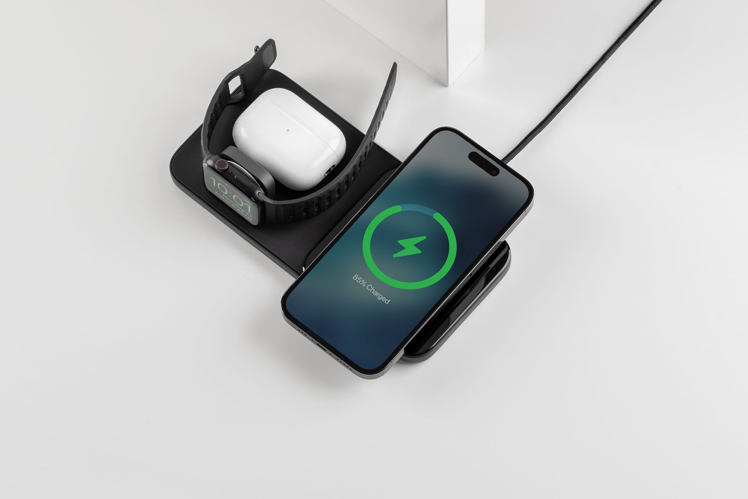 An iPhone, Apple Watch, and AirPods case charging on a black Nomad Base One Max 3-in-1 charger.