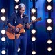 Tracy Chapman performing with a guitar at the Grammys, backdropped by stage lights