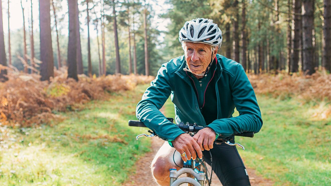 Older man biking in blue jersey outside.