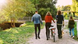 Group of men and women walking through a park bicycle. Friends walking together on a pathway through a park.