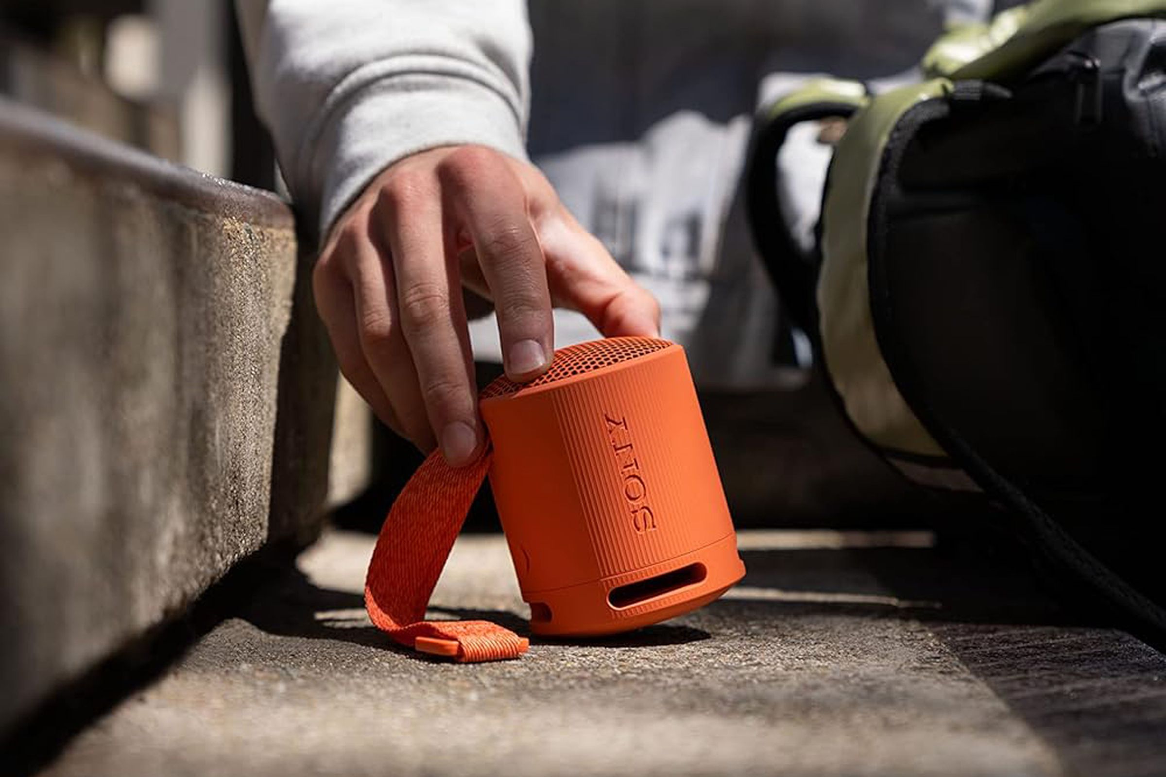 A close-up image of a hand placing an orange version of Sony SRS-XB100 on a set of stairs.