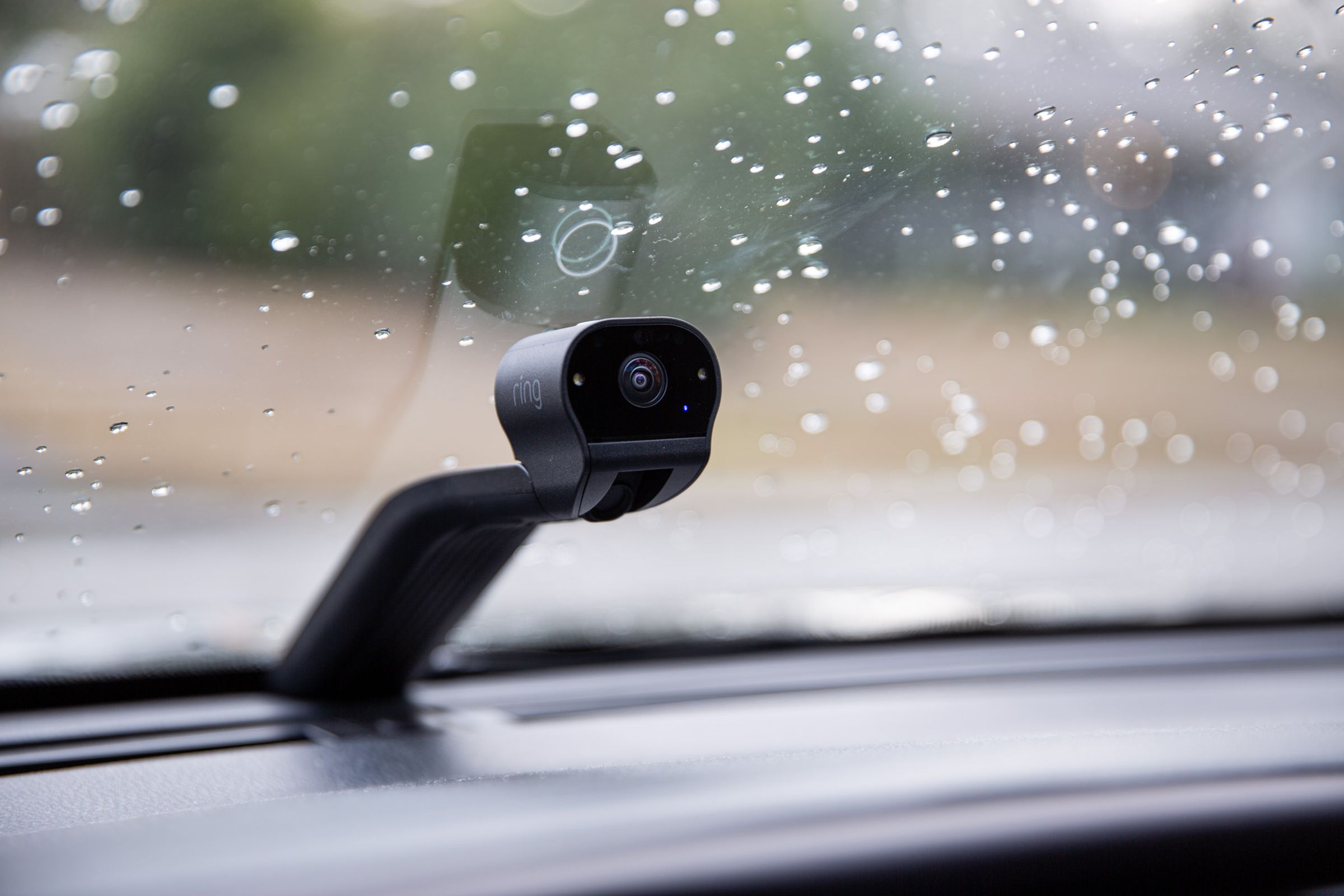 A small camera on top of a long black stand fitted onto a car windshield.