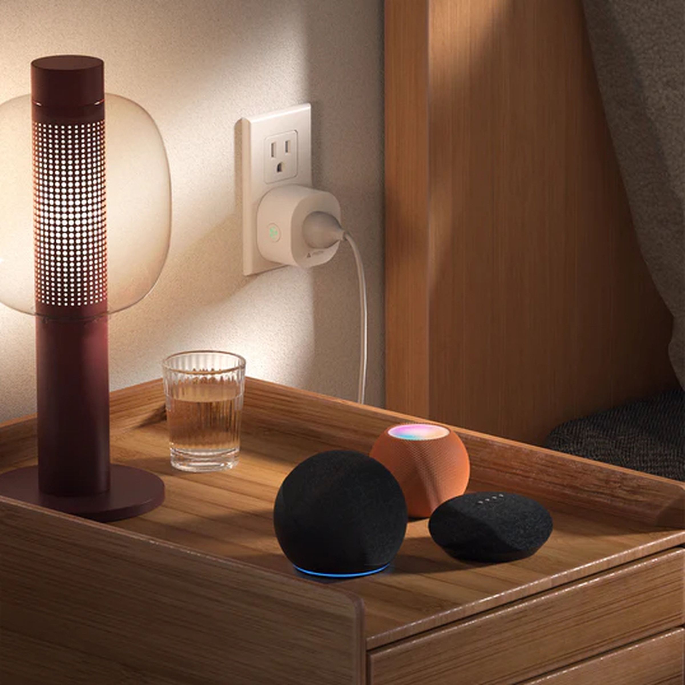 A lamp plugged into a smart plug next to three smart speakers.