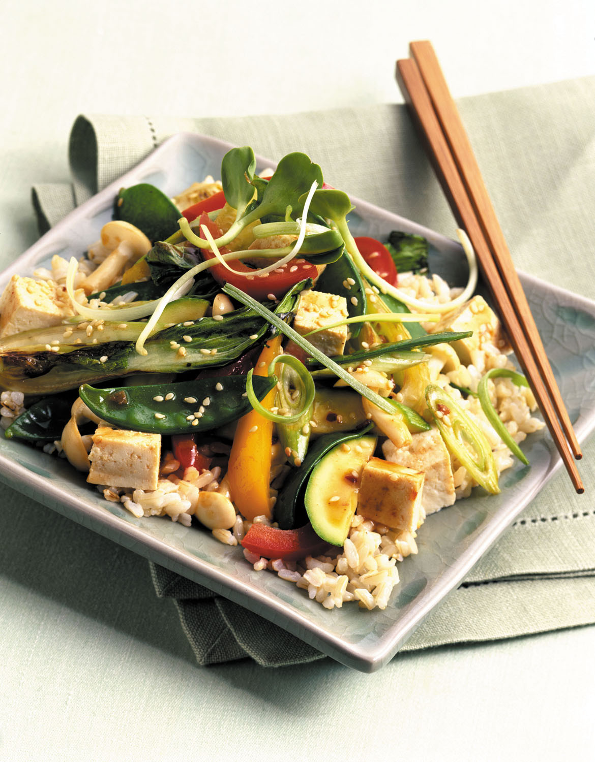 photo of a healthy meal: Chinese stir-fry with tofu, vegetables, and brown rice, served on a square plate with chopsticks set on the side