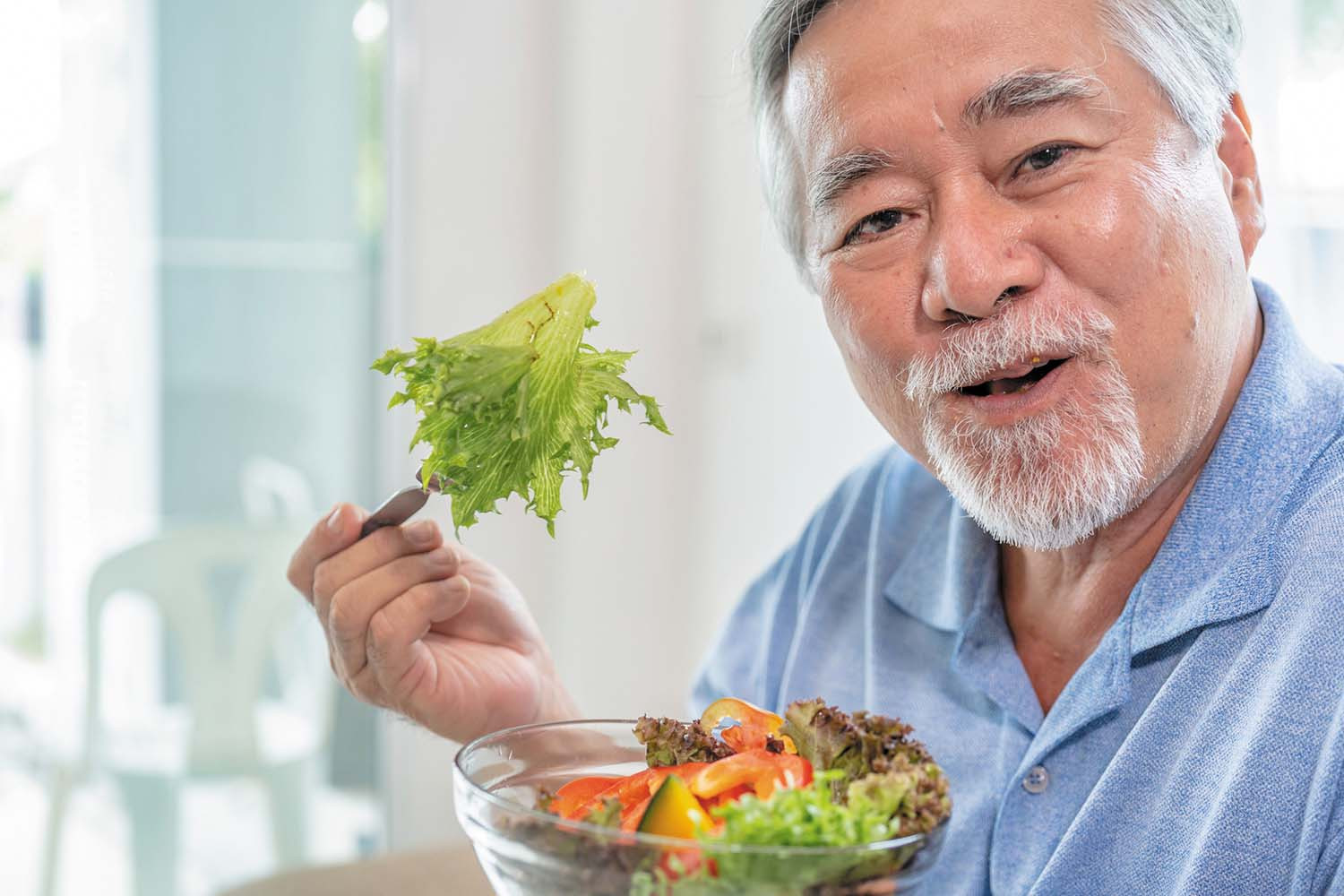 photo of a man holding a glass bowl filled with salad in one hand and a forkful of lettuce from the bowl in the other hand