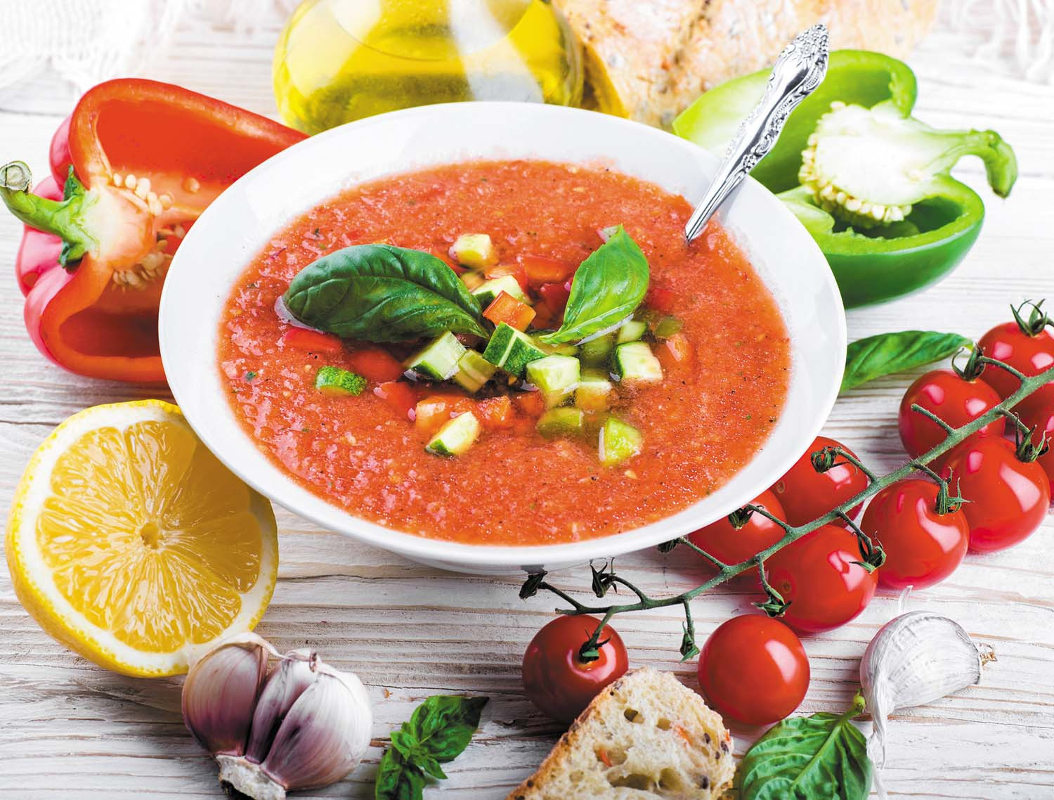 photo of a bowl of tomato soup with herbs on top and a spoon in the bowl