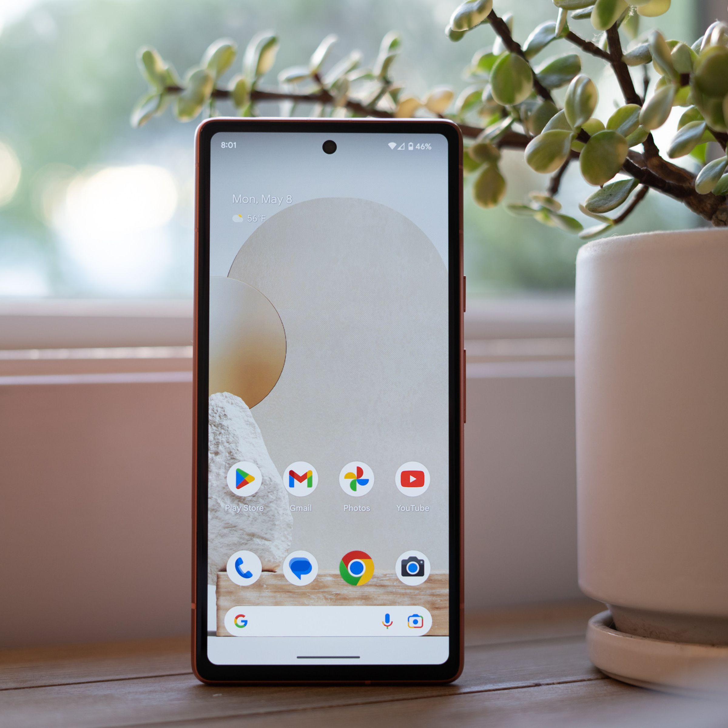 Google Pixel 7A standing upright on a table showing home screen.