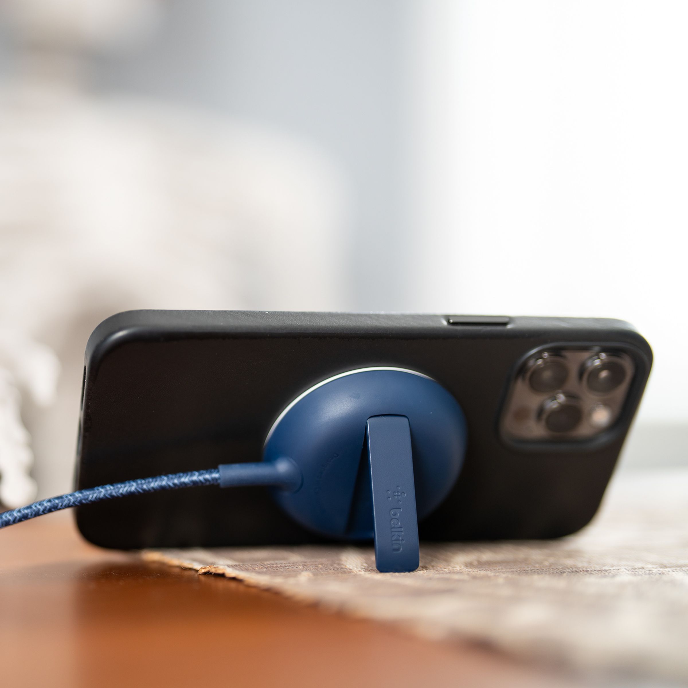 An iPhone propped up horizontally by the kickstand of a Belkin MagSafe charger on a table with a prop skeleton sitting in a chair and looking at the phone.