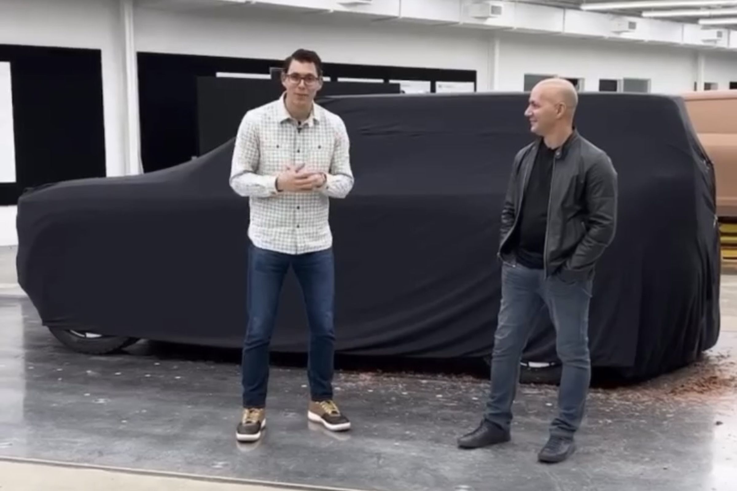 Black cloth covering a clay model of the R2 SUV with CEO RJ Scaringe and lead designer Jeff Hammoud standing in front of it.