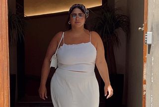 Influencer standing in front of doorway with white two-piece linen set, sunglasses, and white shoulder bag.