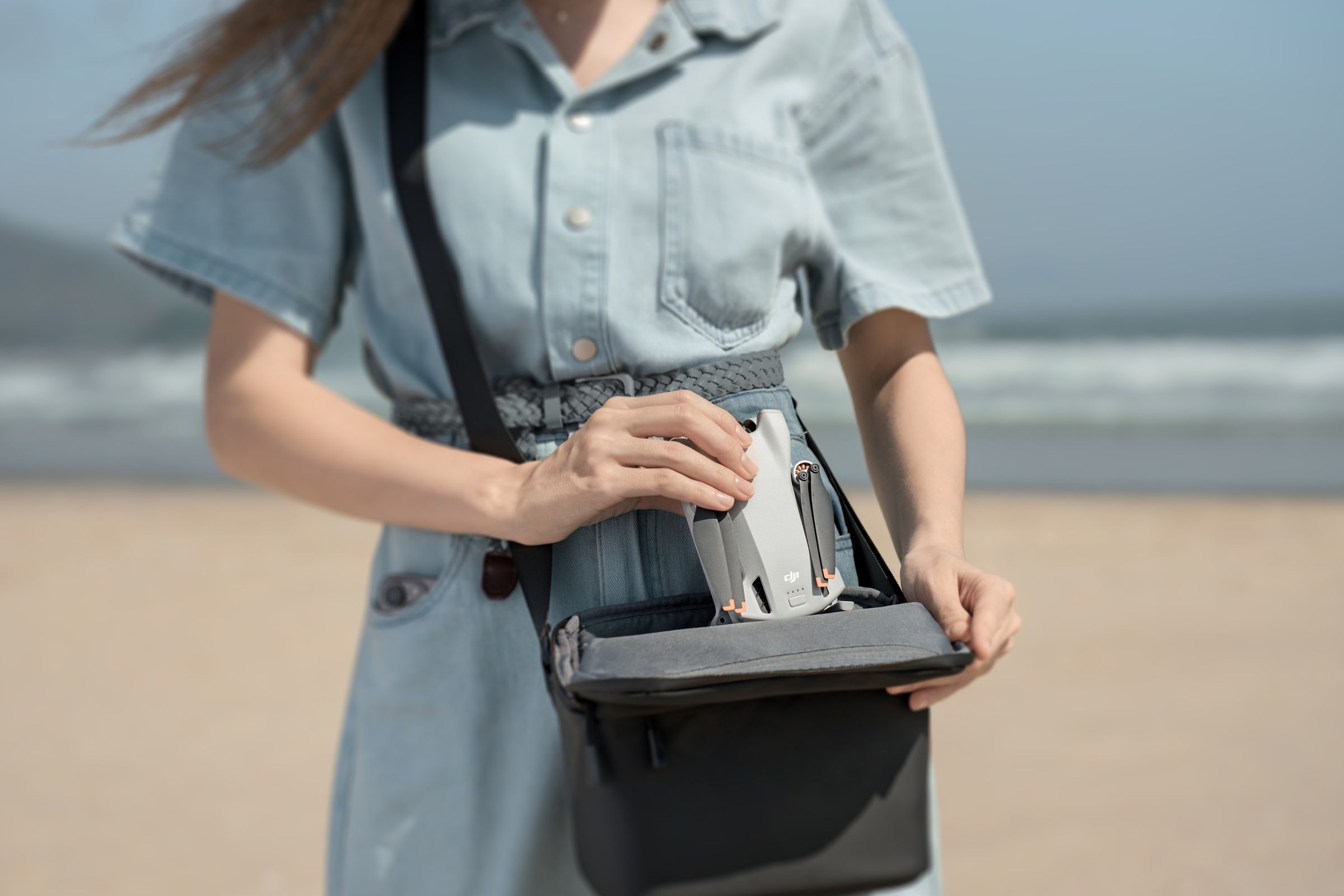 A person on the beach, placing a compacted DJI Mini 3 drone into an average sized handbag.