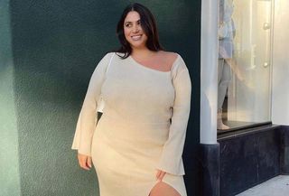 Influencer standing in white knit dress against green wall.