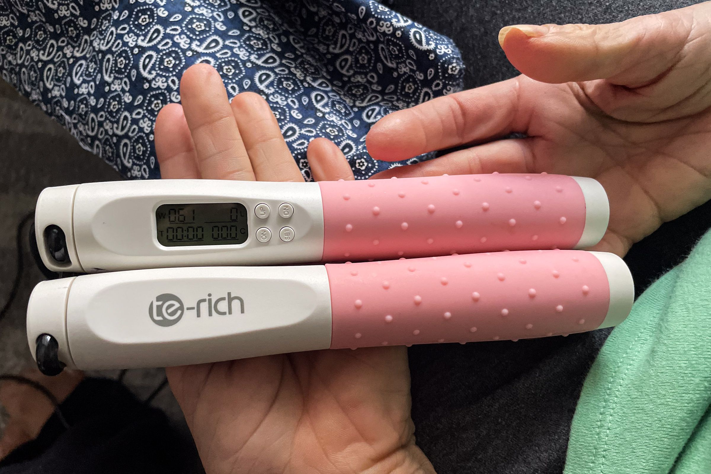 A hand holding the Te-Rich Smart Weighted Jump Rope’s pink handles, with one handle featuring a built-in LCD display with a timer and jump counter.