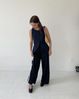 New York fashion influencer Laura Reilly stands in a long denim vest, black Adidas pants, and black flats