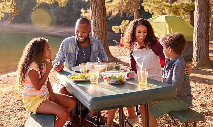 Family of four eating at a table at a campsite outdoors