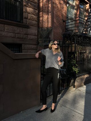 Eliza Huber wearing a gray V-neck sweater with black cigarette pants and black kitten heels.