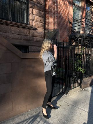 Eliza Huber wearing a gray V-neck sweater with black cigarette pants and black kitten heels.