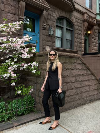 Eliza Huber wearing a black vest and cigarette pants with a black top-handle bag and brown-and-black slingback wedges.