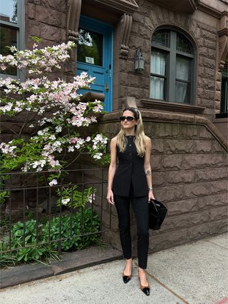 Eliza Huber wearing a black vest and cigarette pants with a black top-handle bag and brown-and-black slingback wedges.